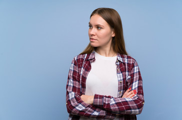 Young woman over blue wall standing and looking side