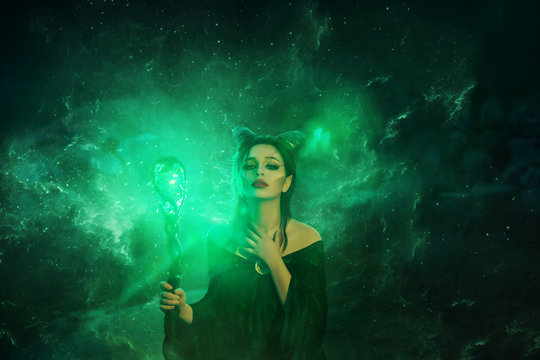 mysterious dark elf got terrible curse, charming girl with horns on head and glowing sparkling magic stick in hands, damned lady in green electric fire puts her hand on neck, creative art photo