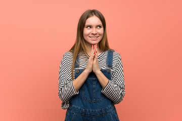 Young woman with overalls over pink wall scheming something