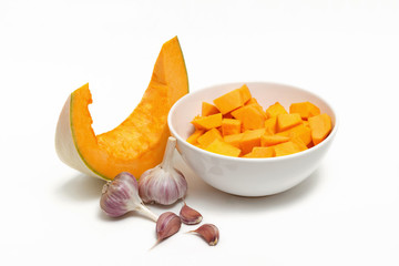 Pumpkin sliced in a white plate and garlic on a white background.
