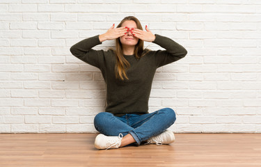 Young woman sitting on the floor covering eyes by hands