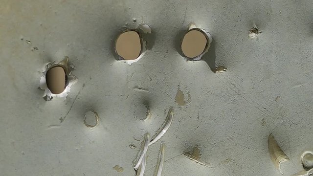 A steady, extreme close up shot of a few bullet holes in a silver metal.