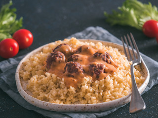 Bulgur dish idea and recipe. Bulgur with homemade roasted beef meatballs on dark blue background. Copy space for text. Shallow DOF