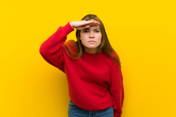 Young woman over yellow wall looking far away with hand to look something