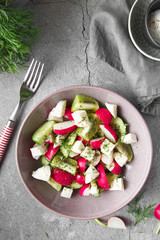 Radish, cucumber, kiwi, cheese and dill salad in a bowl on gray grunge concrete background. Seasonal Cooking, food styling.
