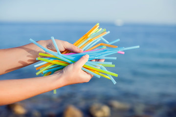 Close Up Of Hand Holding Plastic Straws Polluting Beach. Environmental pollution concept