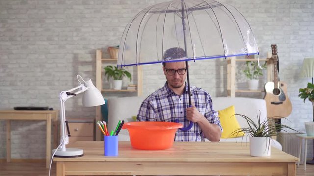 Disgruntled young man under an umbrella during a flood in the apartment