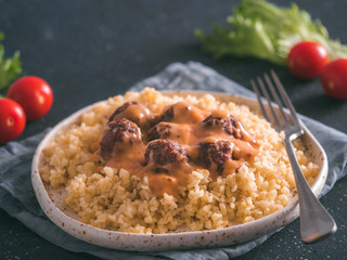 Bulgur dish idea and recipe. Bulgur with homemade roasted beef meatballs on dark blue background. Copy space for text. Shallow DOF