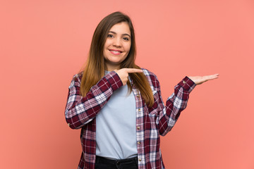 Young girl over pink wall holding copyspace imaginary on the palm to insert an ad
