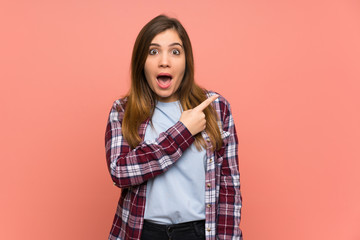 Young girl over pink wall surprised and pointing side