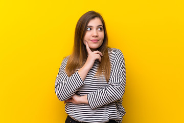 Young girl over yellow wall thinking an idea while looking up