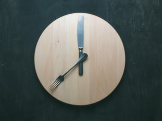 Intermittent fasting and skip breakfast concept - empty wooden round tray or trencher with cutlery...