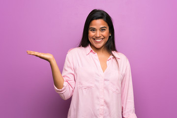 Young Colombian girl over purple wall holding copyspace imaginary on the palm to insert an ad