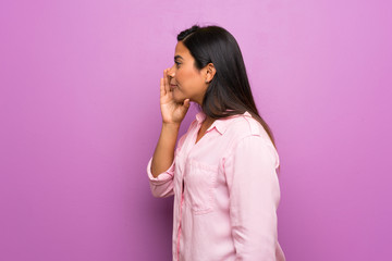 Young Colombian girl over purple wall shouting with mouth wide open to the lateral