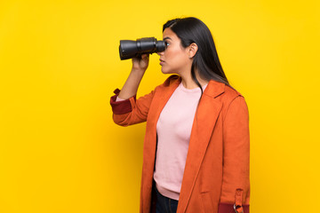 Young Colombian girl over yellow wall and looking in the distance with binoculars