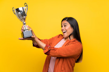 Young Colombian girl over yellow wall holding a trophy