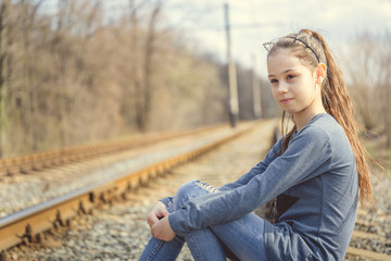 Pensive girl sitting on railway. Side view of young thoughtful girl sitting on rail and looking away in nature	