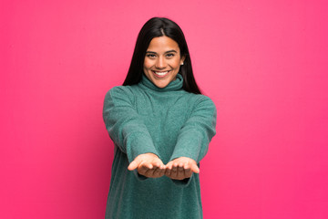 Young Colombian girl with green sweater holding copyspace imaginary on the palm to insert an ad