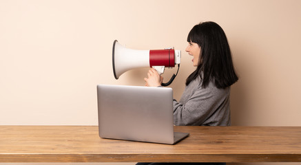 Young woman working with her laptop shouting through a megaphone