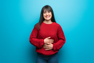 Obraz premium Woman with red sweater over blue wall smiling a lot