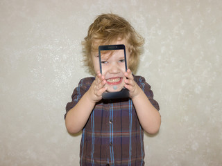 A boy kid looks into the camera of a smartphone, shows the screen with his digital photo. Toddler smiles at the camera and takes a selfie.