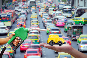 Left hands of men who were holding an automatic nozzle to make refill oil on yellow toy car on right hand with traffic jam on blurred background, industry oil and gas energy concept