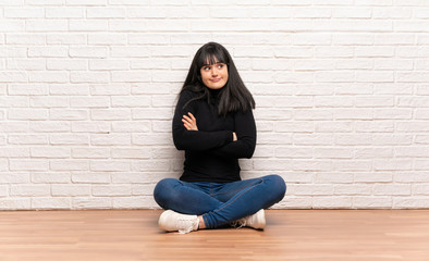 Woman sitting on the floor making doubts gesture while lifting the shoulders