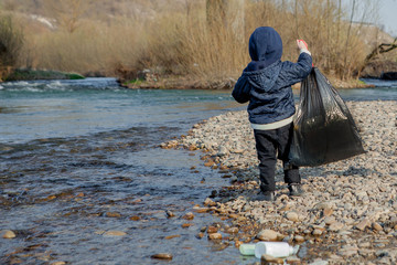 Save environment concept, a little boy collecting garbage and plastic bottles on the beach to dumped into the trash.