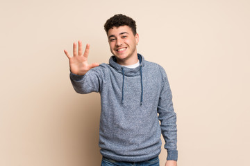 Young man over isolated wall counting five with fingers