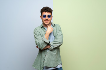 Fototapeta premium Young man over blue and green background with glasses and smiling