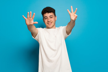 Young man over blue background counting eight with fingers