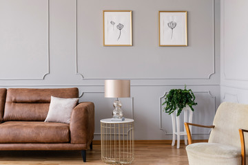 Real photo of a glamour living room interior with a sofa, lamp on a table and graphics on a wall