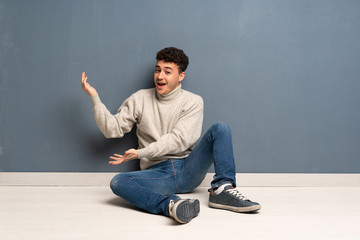 Young man sitting on the floor extending hands to the side for inviting to come