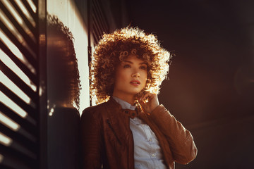 Portrait of a young woman in a brown leather jacket with blond afro curly hair on the street