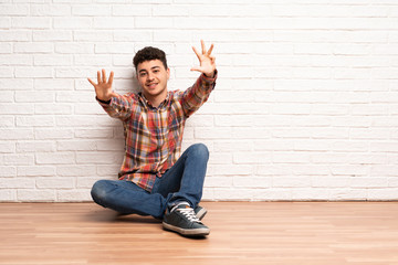 Young man sitting on the floor counting nine with fingers