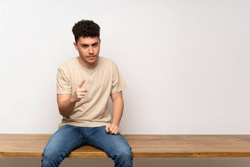Fototapeta premium Young man sitting on table frustrated and pointing to the front