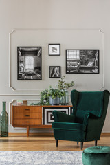 Emerald green armchair in elegant living room with black and white photos on grey wall and retro cabinet