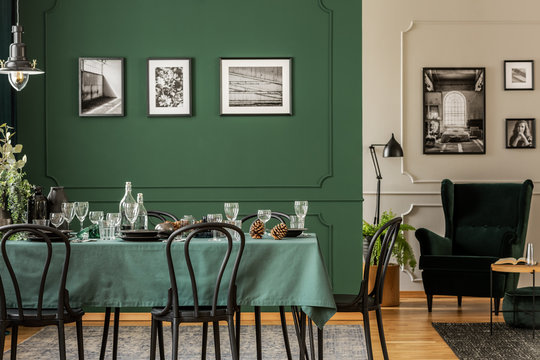 Black and white posters on green wall of stylish dining room interior with log table with wine glasses, plates and cones