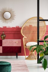 Trendy living room interior with wicker peacock chair and handmade pastel pink and burgundy chest of drawers