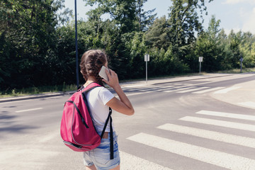 Girl with backpack using smartphone while walking through pedestrian crossing