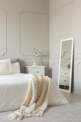 Mirror in white frame on grey wall of stylish scandinavian bedroom interior with king size bed with cozy blanket