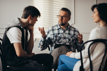 Psychologist talking to depressed teenager and his mum during therapy session - obrazy, fototapety, plakaty
