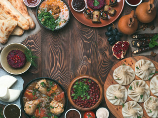 View from above of georgian cuisine on brown wooden table.Traditional georgian food-khinkali,kharcho,chahokhbili,phali,lobio and local sauces - tkemali, satsebeli, adzhika.Top view.Copy space for text - obrazy, fototapety, plakaty