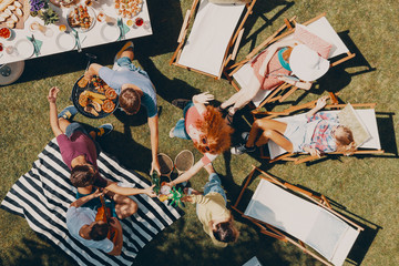 High angle on friends making toast and relaxing on sunbeds during outdoor party