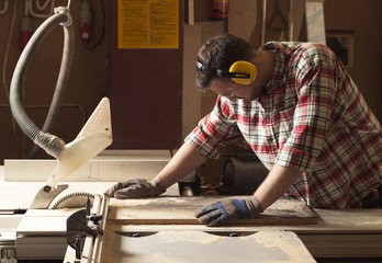 Handyman with protective headphones and gloves during woodwork in the workshop