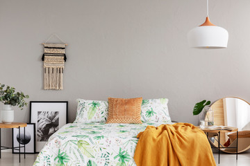 Orange blanket on floral duvet in stylish bedroom interior with handmade macrame, black and white...