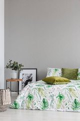 Copy space on the empty grey wall of cozy bedroom with leaf pattern on the bedding and olive green pillows