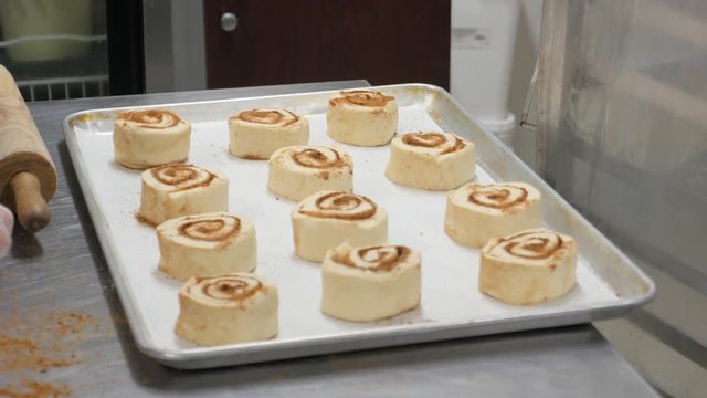 woman places last cinnamon rolls on tray to bake. Woman loads tray with cinnamon rolls.