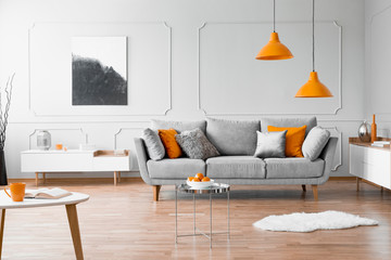 Real photo of a modern living room interior with a sofa, orange lamps and painting