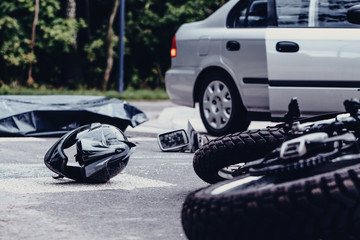 Motorcycle helmet on the street after terrible car crash, black bag with corpse and car with open door next to it